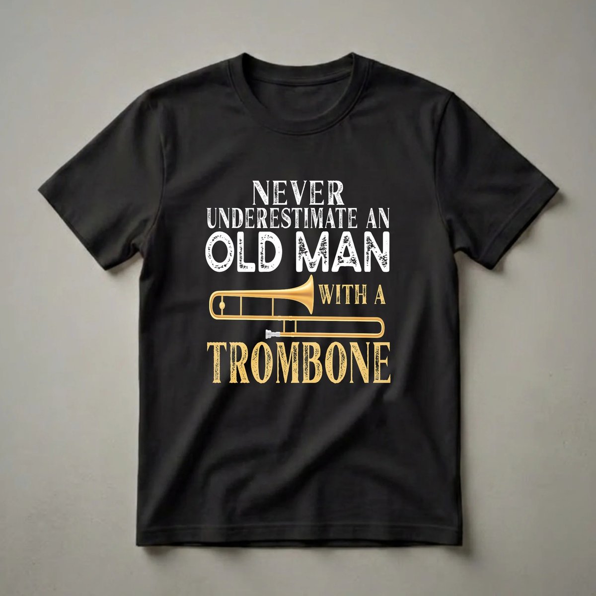 Black t-shirt with white distressed text 'NEVER UNDERESTIMATE AN OLD MAN' above a golden trombone illustration and distressed golden text 'WITH A TROMBONE'.