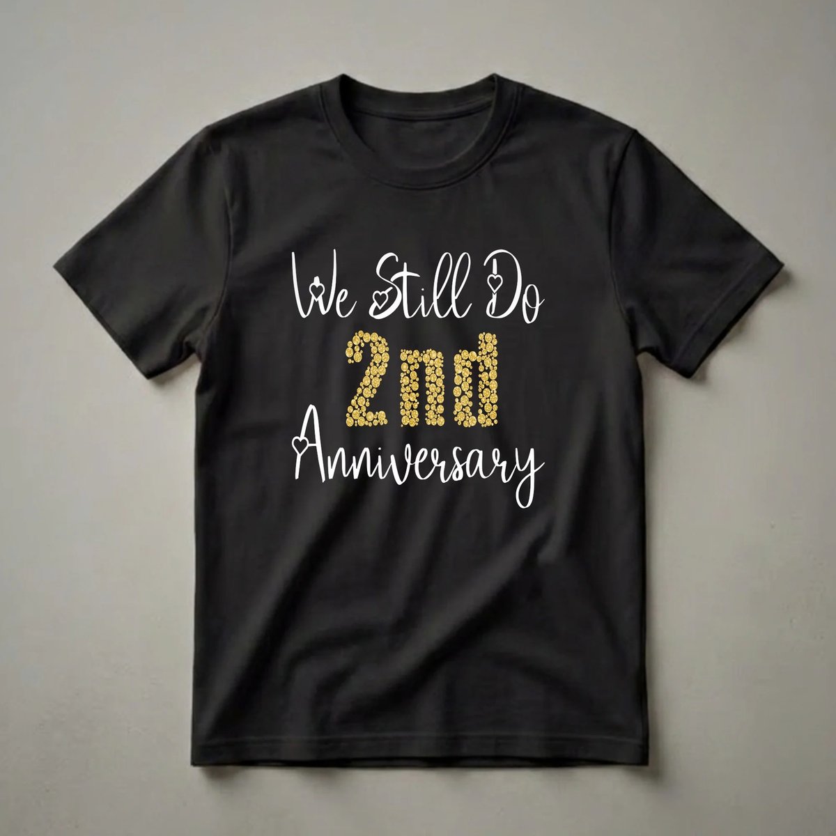 Black t-shirt with white script text 'We Still Do' and 'Anniversary', and gold glitter numbers spelling out '2nd'.