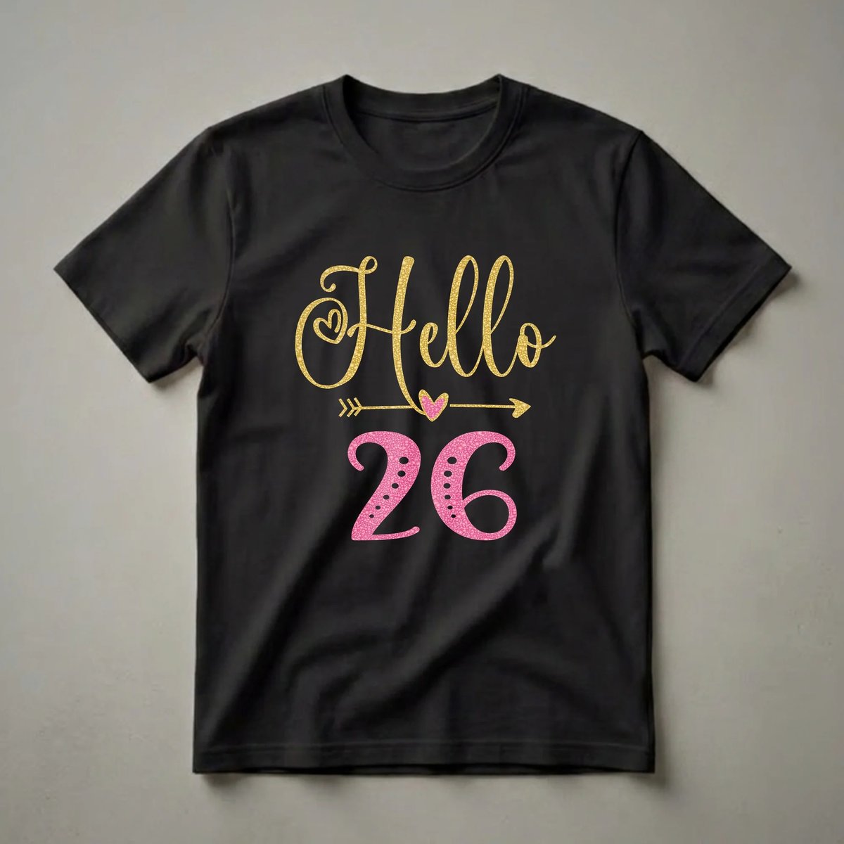 Black t-shirt with gold glitter text 'Hello' and pink textured number '26', with a gold arrow and pink heart graphic.