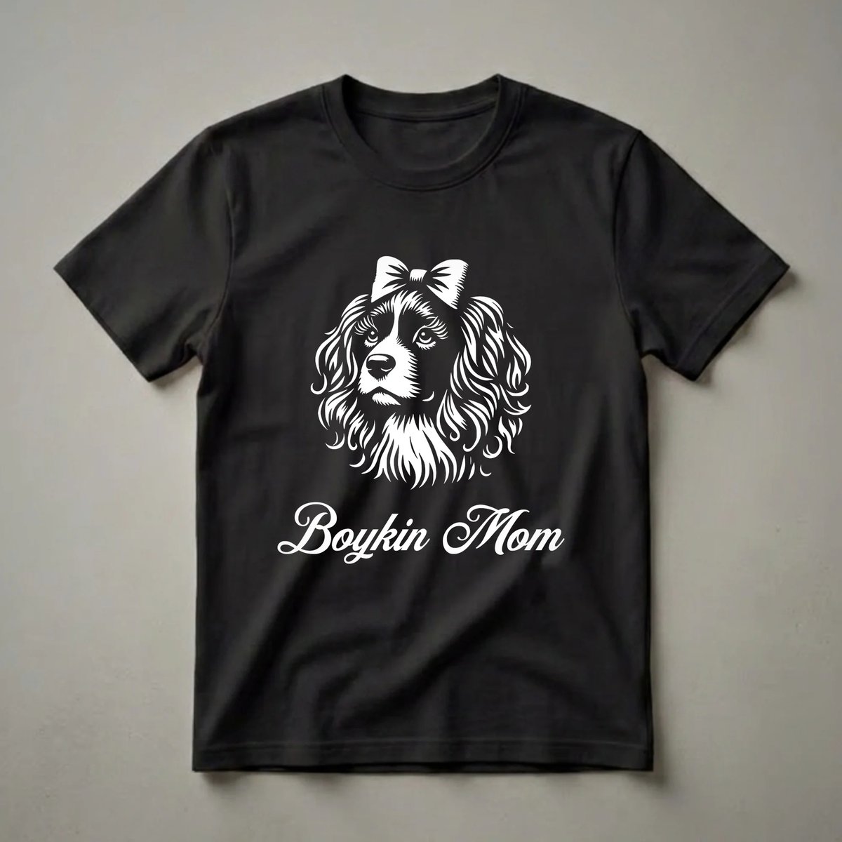 White graphic of a Boykin Spaniel dog wearing a bow, with the text 'Boykin Mom' below, on a black t-shirt.