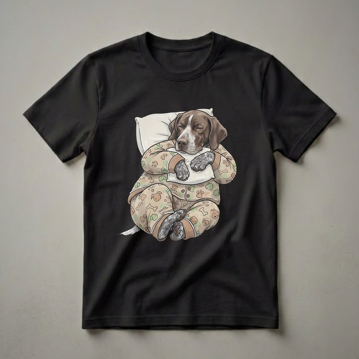 A brown and white German Shorthaired Pointer dog wearing pajamas and sleeping on a pillow, depicted on a light tan t-shirt with a pattern of paw prints and bones.