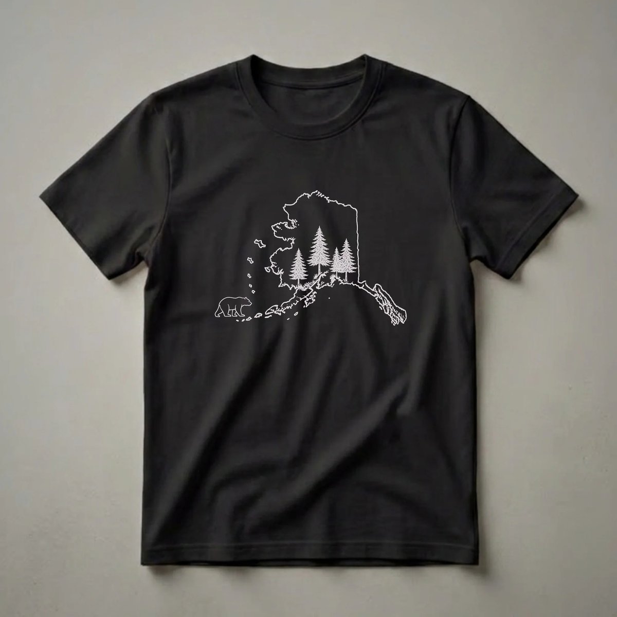 Black t-shirt with a white outline of the state of Alaska, featuring a sketch of pine trees and a walking bear inside.