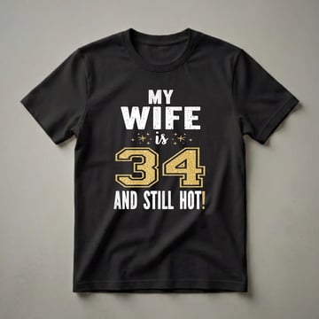 Black t-shirt with white distressed text reading "MY WIFE is" and "AND STILL HOT!". The number "34" is prominently displayed in a large gold glitter font with a black outline.