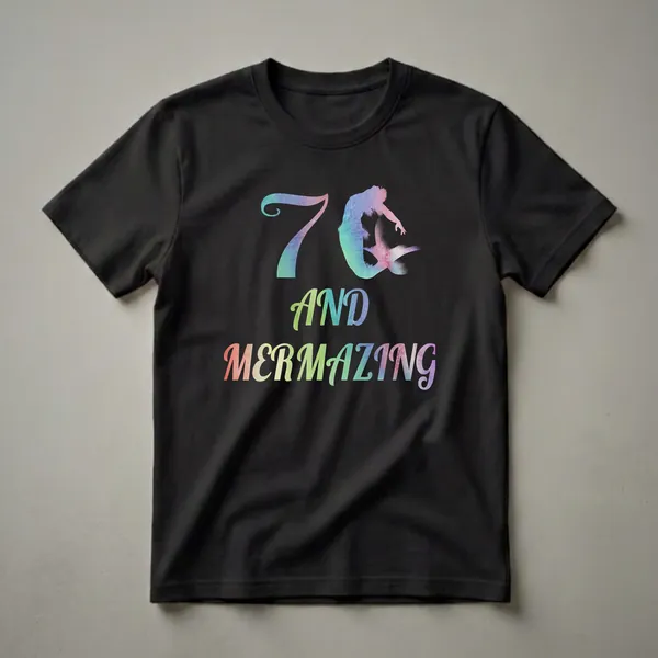 Black t-shirt with a watercolor graphic featuring the number 7 and a mermaid silhouette, followed by the words 'AND MERMAZING' in colorful watercolor lettering.