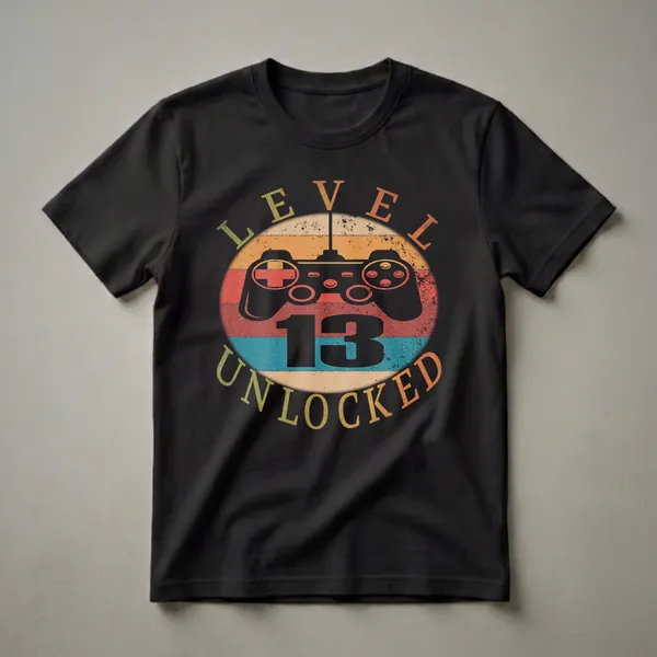 Black t-shirt with a graphic design featuring a vintage video game controller and the text 'LEVEL 13 UNLOCKED' in distressed lettering against a circular background of retro stripes.