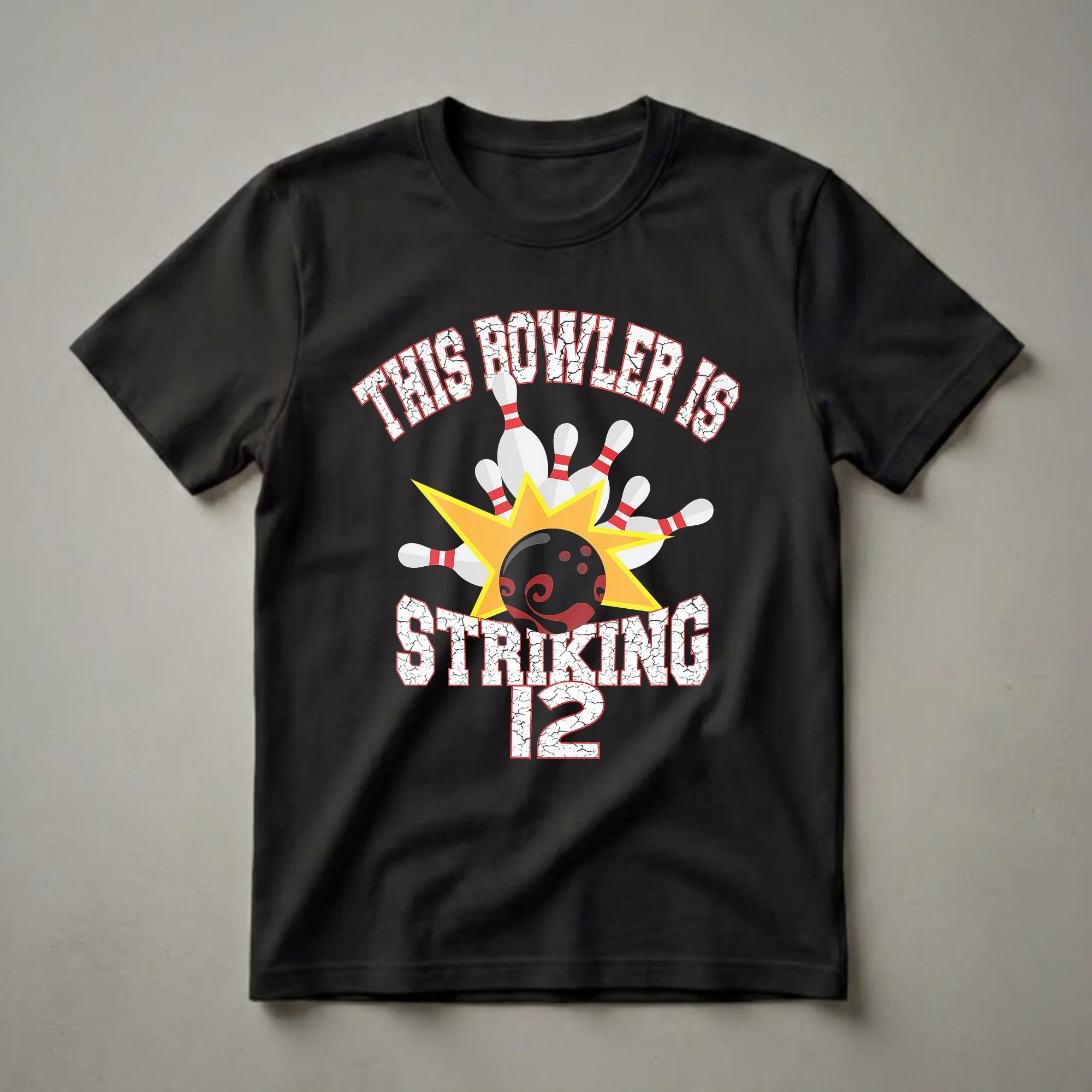 Black t-shirt with white and red distressed text that reads 'THIS BOWLER IS STRIKING 12', featuring a graphic of a bowling ball hitting pins with a yellow starburst.