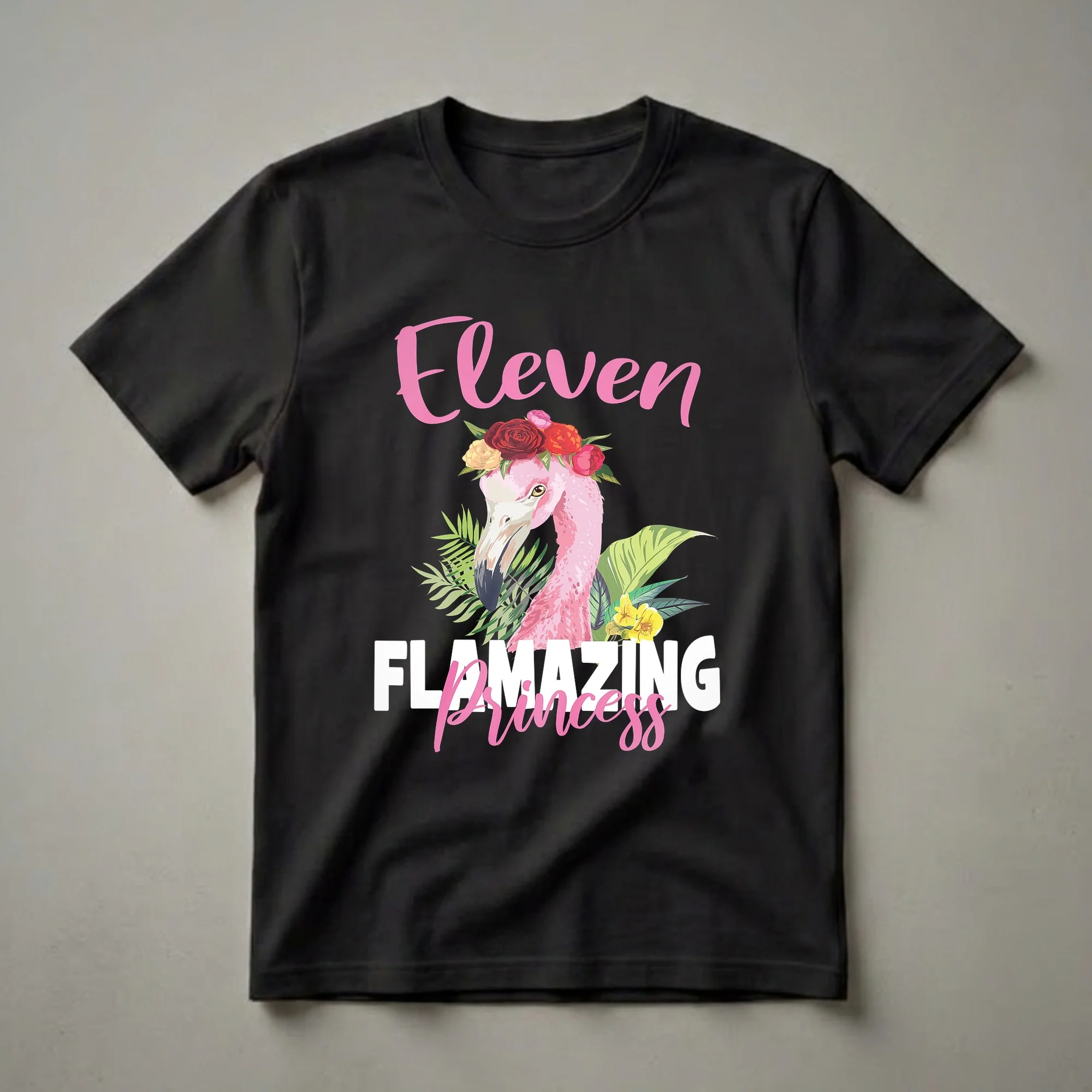 White shirt design with 'Eleven' in pink brush script, a floral-crowned pink flamingo surrounded by tropical leaves and yellow flowers, and 'Princess' in pink cursive below.