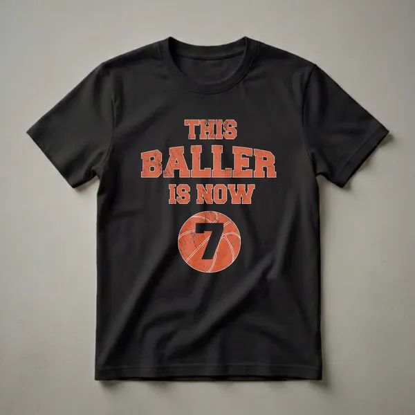 Black t-shirt with distressed orange text reading 'THIS BALLER IS NOW' above a distressed basketball graphic with the number 7 in black.