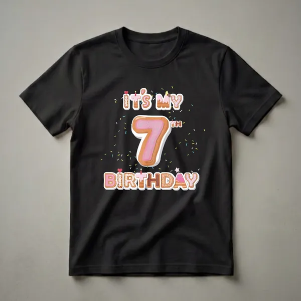 Black t-shirt featuring donut-themed letters spelling 'It's My Birthday' and a large donut-shaped number '7' with pink frosting and sprinkles, surrounded by colorful confetti.