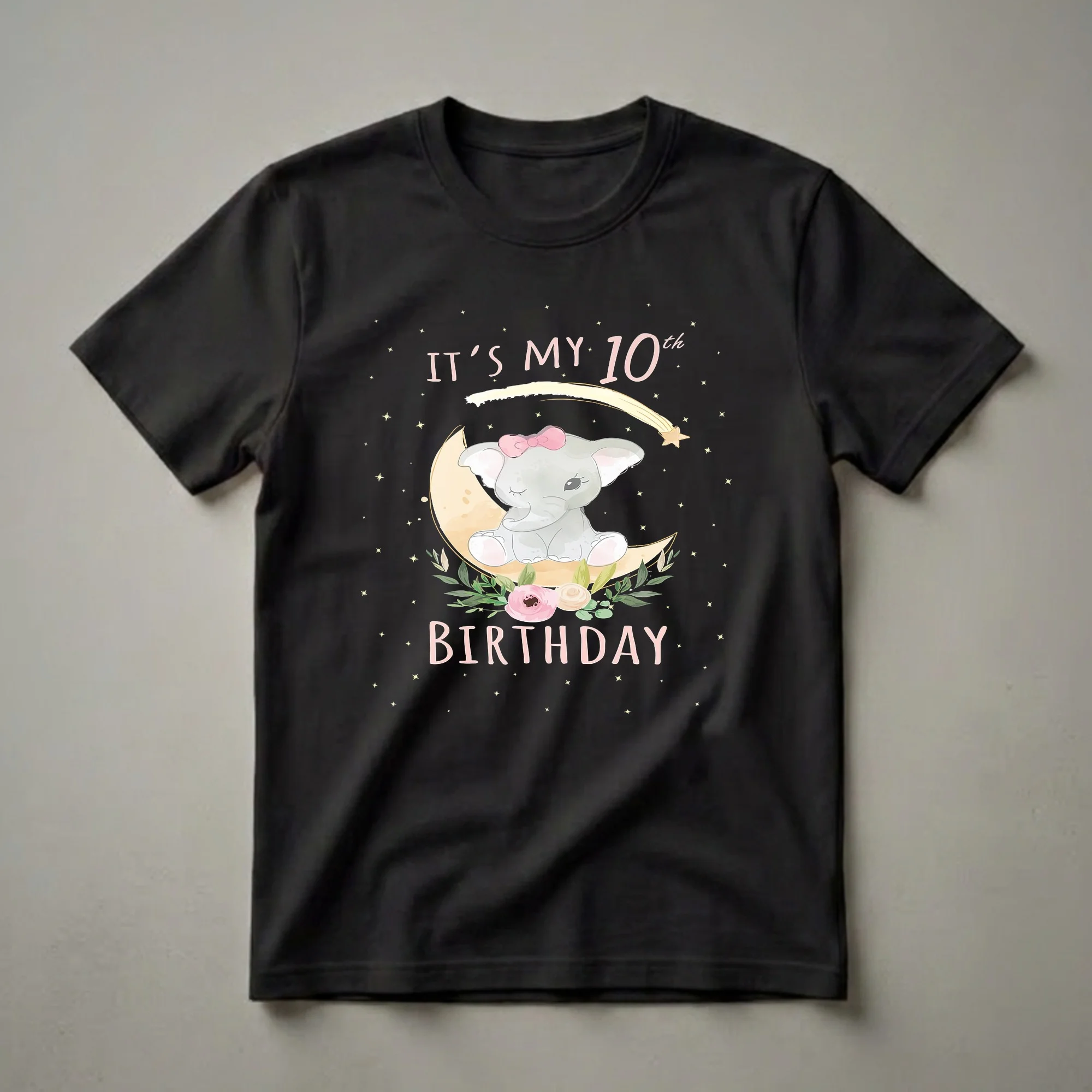 Black t-shirt with a watercolor illustration of a baby elephant wearing a pink bow, sitting on a crescent moon surrounded by flowers, leaves, stars, and the text 'IT'S MY 10th BIRTHDAY'.