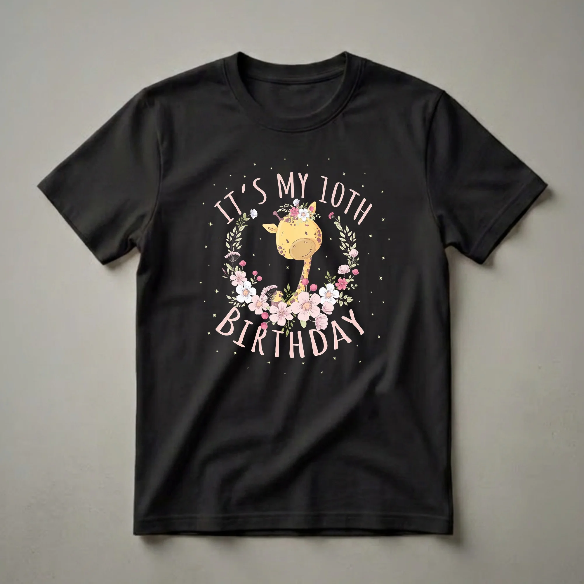 Black t-shirt featuring a cartoon giraffe wearing a floral crown, with pink text reading 'It's My 10th Birthday' and surrounded by flowers and yellow stars.