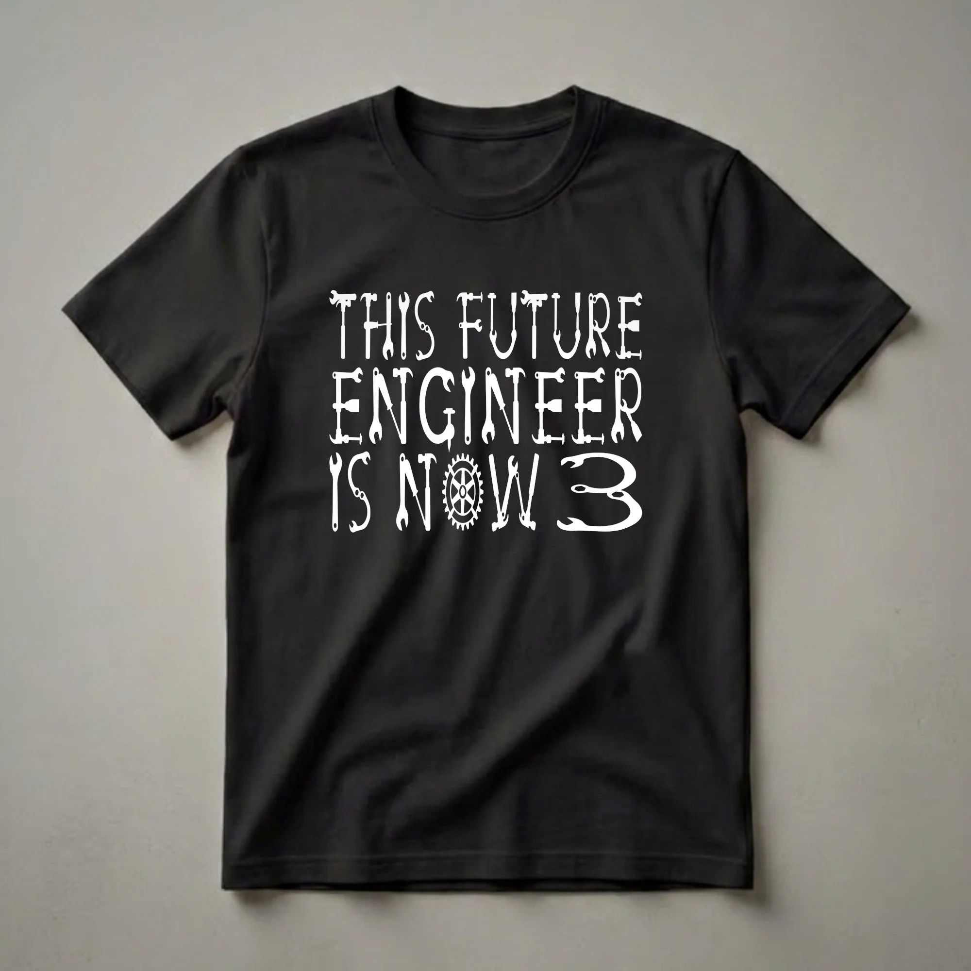 Black t-shirt with white text that reads 'THIS FUTURE ENGINEER IS NOW 3', with letters and numbers constructed from various tools like wrenches, hammers, and a gear.