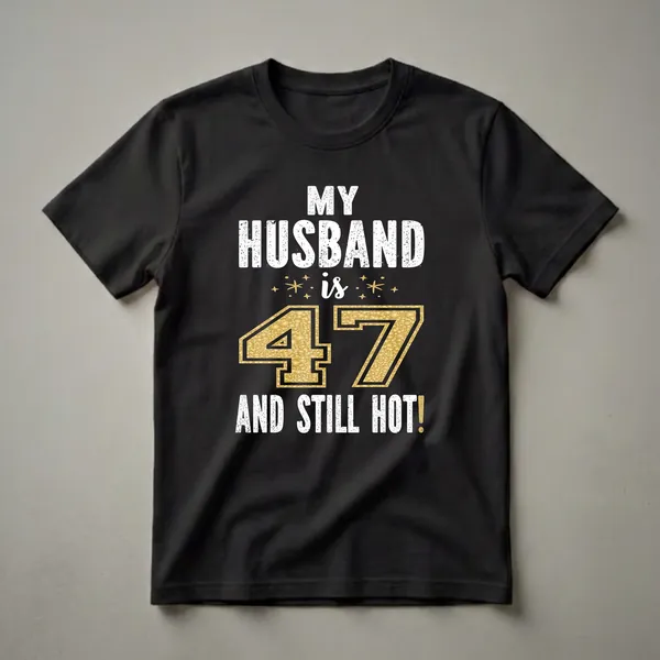 Black t-shirt with white distressed text reading 'MY HUSBAND IS 47 AND STILL HOT!' and a large gold glitter number 47 with sparkling accents.