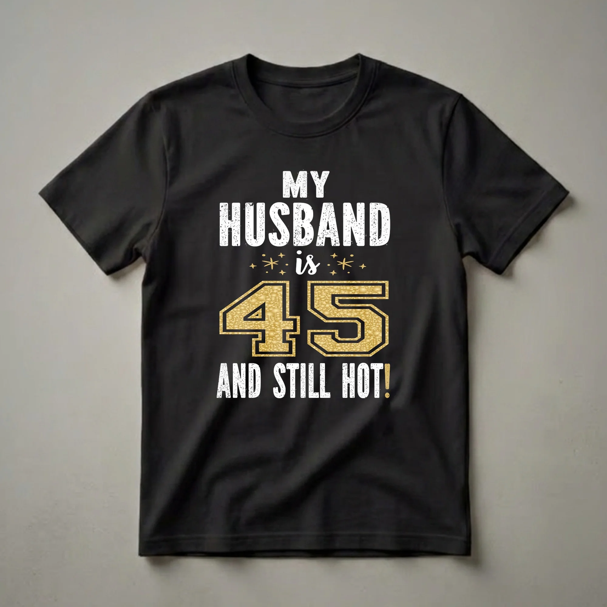 Black t-shirt with white distressed text reading 'MY HUSBAND IS' and 'AND STILL HOT!', with a large gold glitter textured number '45' in the center.