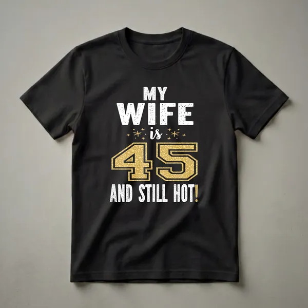 Black t-shirt with white distressed text reading "MY WIFE is 45 AND STILL HOT!". The number 45 is large and filled with a gold glitter texture, with small gold stars around the word 'is'.