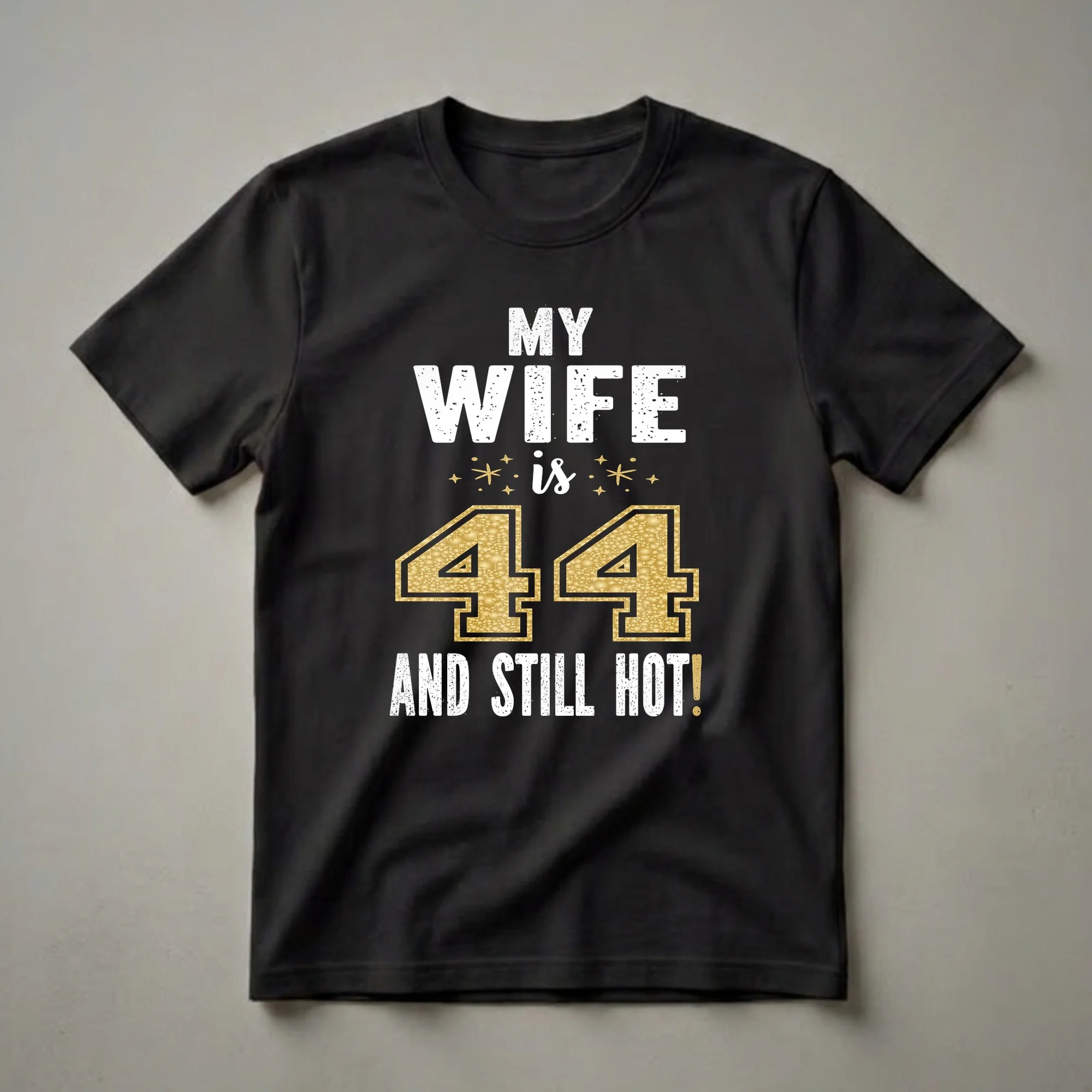 Black t-shirt with white distressed text that reads "MY WIFE is 44 AND STILL HOT!" with a large glitter gold number 44 and gold stars.