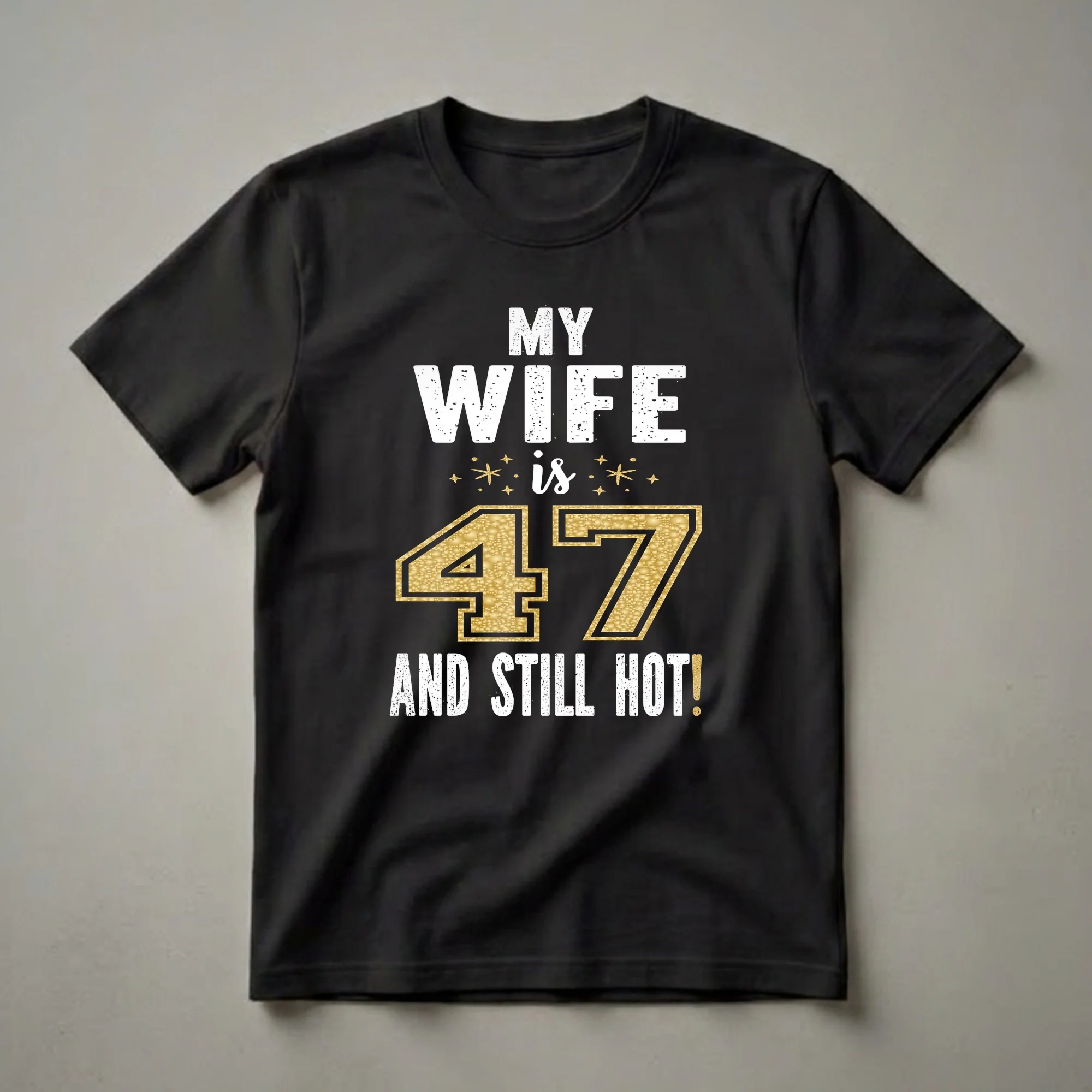 Black t-shirt with white distressed text reading 'MY WIFE is 47 AND STILL HOT!' and a gold glitter textured number 47 with small gold stars.