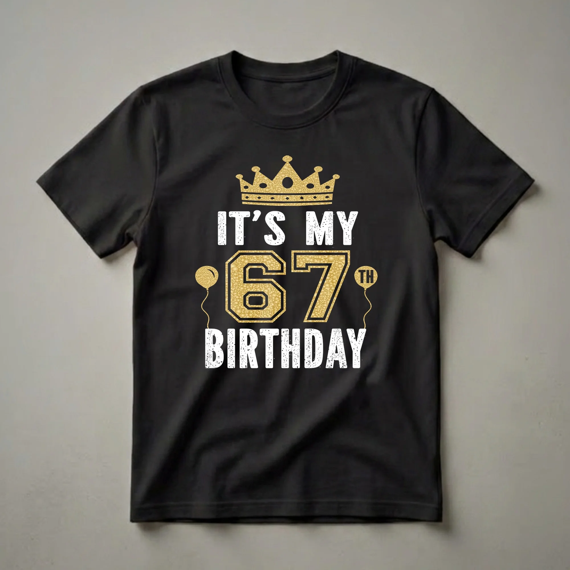 Black t-shirt with a golden crown, white distressed text reading 'IT'S MY', large gold textured '67', two golden balloons, and white distressed text reading 'BIRTHDAY'.