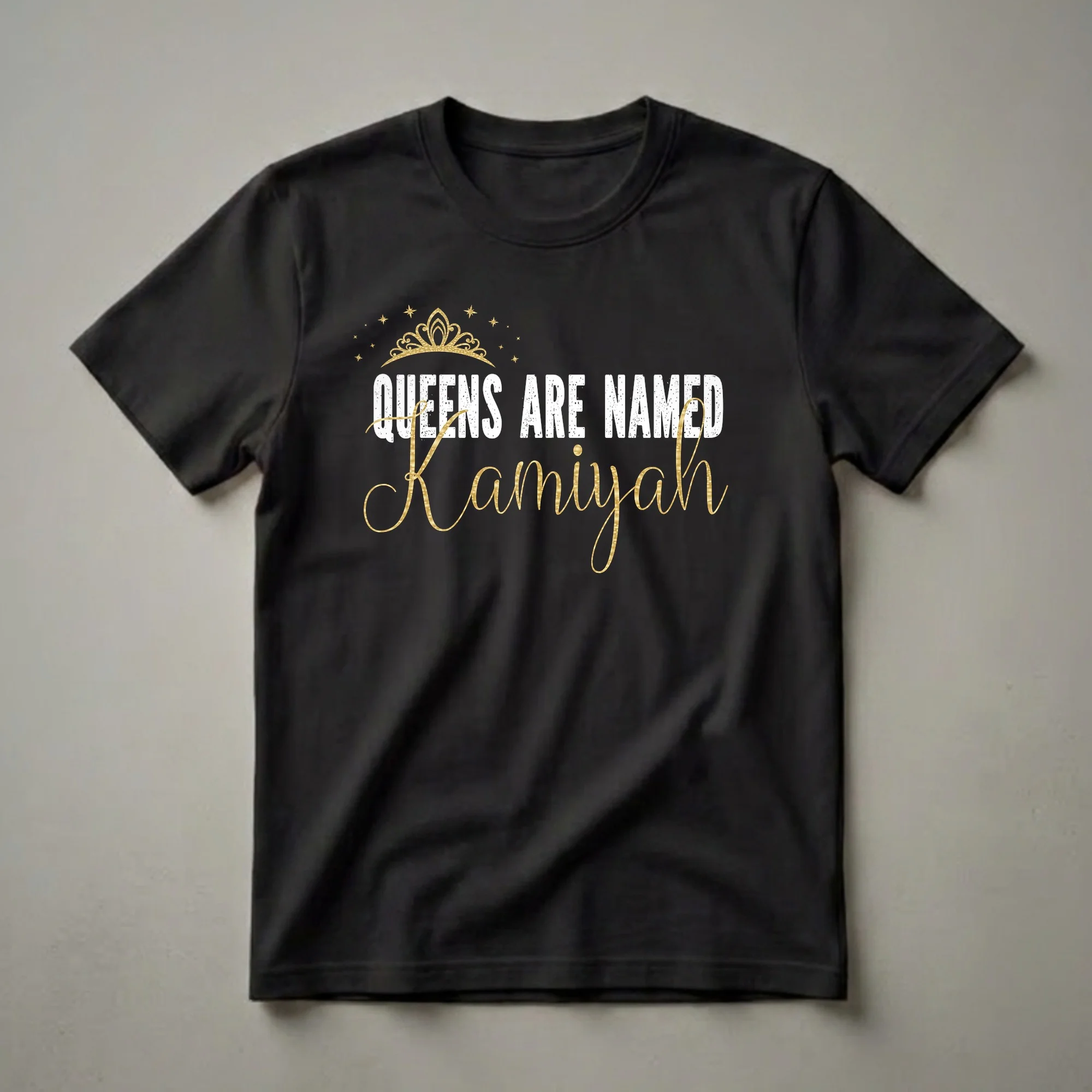 Black t-shirt with white distressed text 'QUEENS ARE NAMED' above a gold script name 'Kamiyah', topped with a gold crown and scattered gold stars.