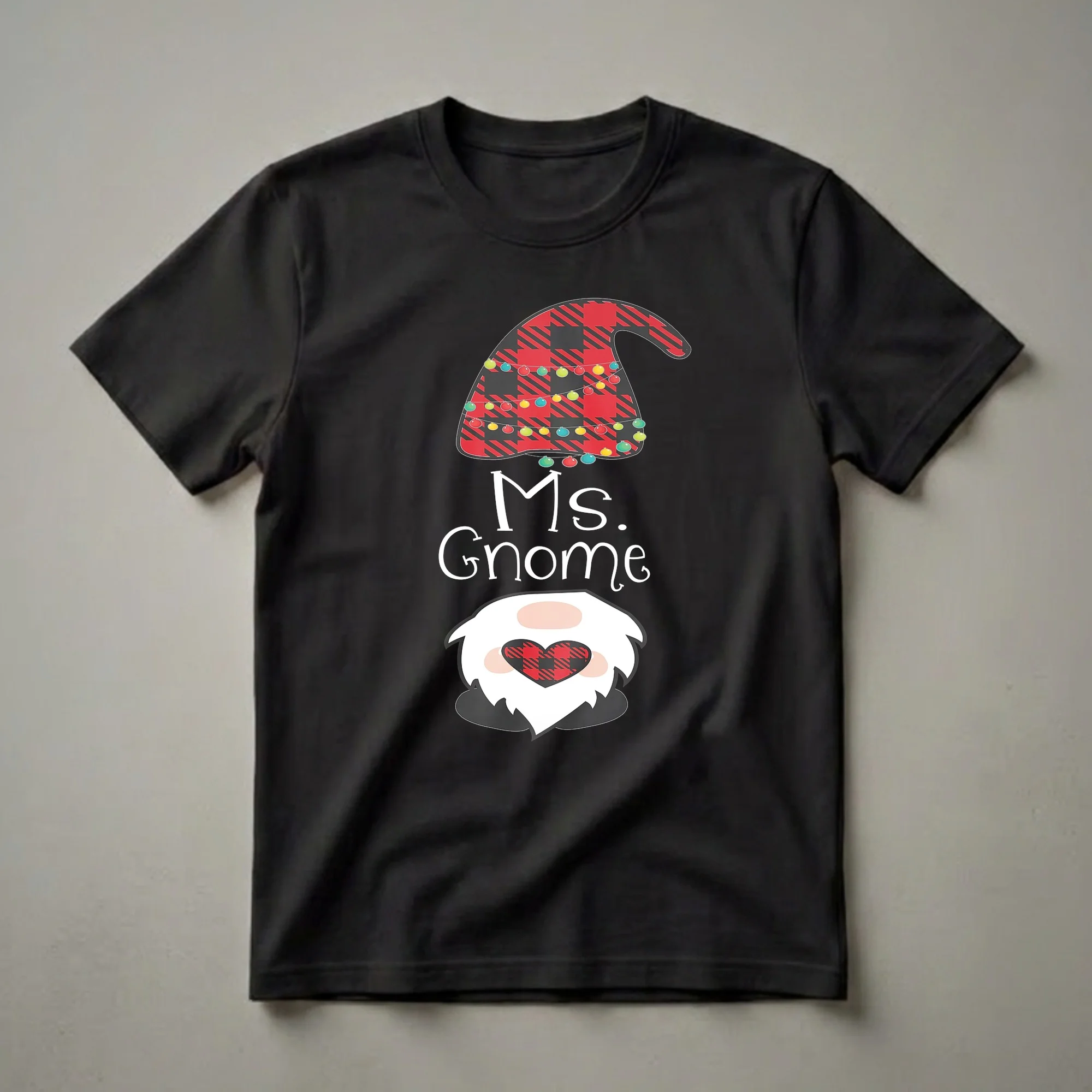A black t-shirt featuring a cartoon Ms. Gnome character with a red and black buffalo plaid hat decorated with colorful Christmas lights and a matching plaid heart.