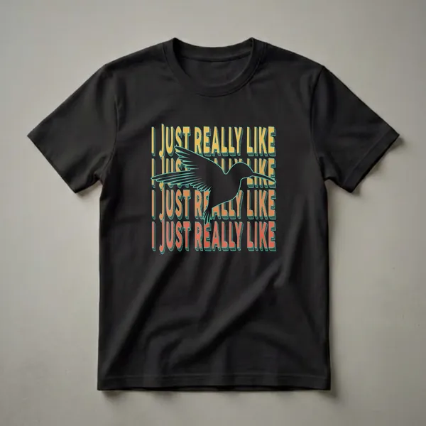 Black graphic t-shirt featuring a silhouette of a hummingbird in flight, with repeating text 'I JUST REALLY LIKE' in retro yellow and orange font with teal outlines.