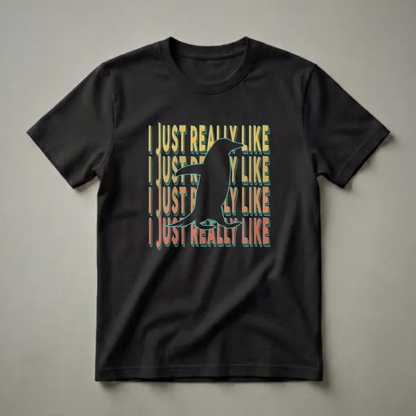 Black graphic t-shirt featuring a silhouette of a penguin in flight, with repeating text 'I JUST REALLY LIKE' in retro yellow, orange, and teal font.