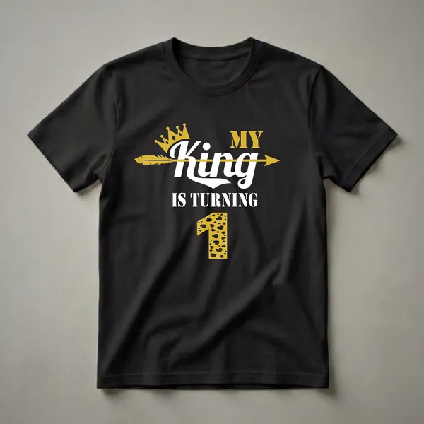 Black t-shirt with gold crown, arrow, and text 'MY King IS TURNING 1'. The number 1 is gold with a leopard print and black heart pattern.