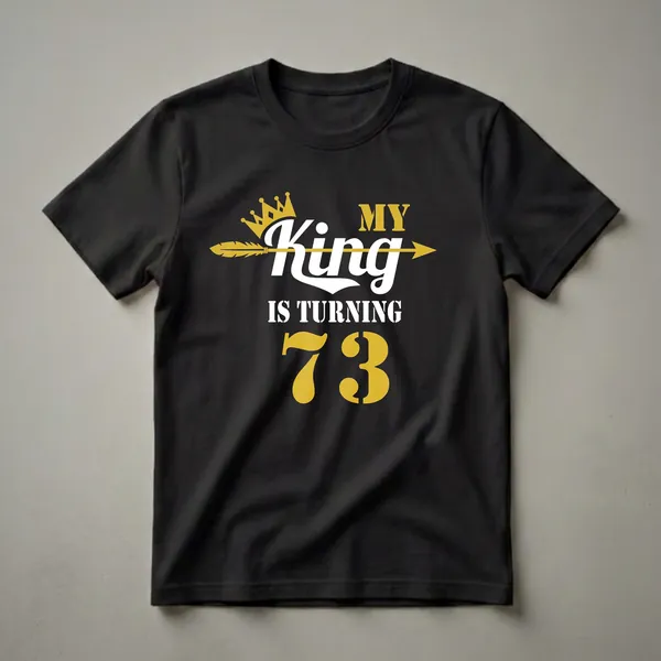Black t-shirt with gold and white text that reads 'MY KING IS TURNING 73', featuring a gold crown and a gold arrow.