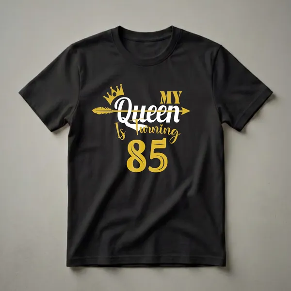 Black t-shirt with gold and white text that reads 'My Queen Is Turning 85' with a gold crown and arrow graphic.