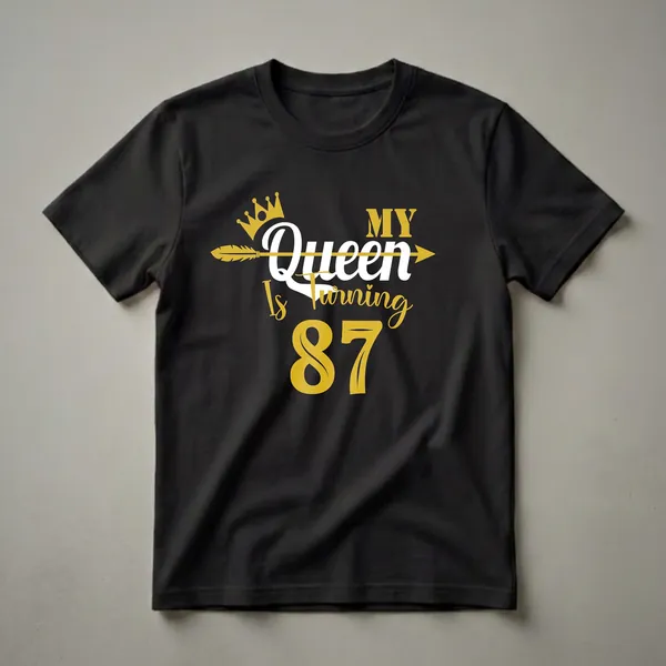 Black t-shirt with gold and white text that reads "MY Queen Is Turning 87" with a gold crown and arrow graphic.