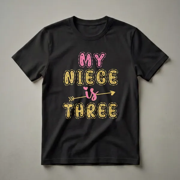 Black t-shirt with the text 'MY NIECE is THREE' in large, glitter-effect pink and gold bubble letters, accented with hearts and a gold arrow.