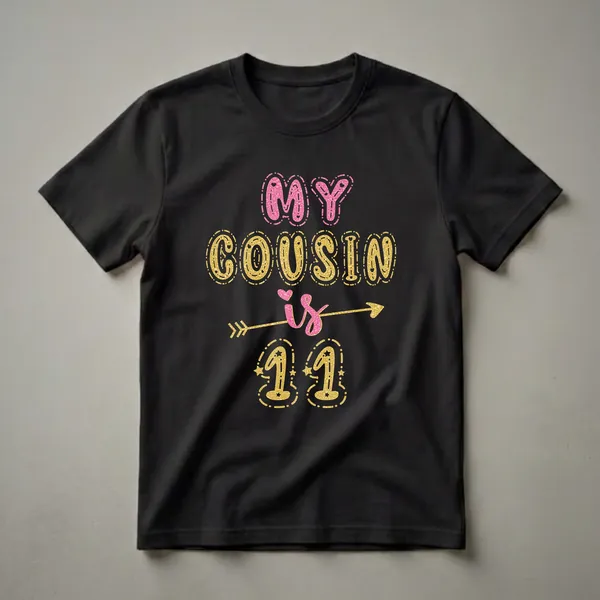 Black t-shirt with glittery pink and gold text that reads 'MY COUSIN is 11' with decorative elements and stars.