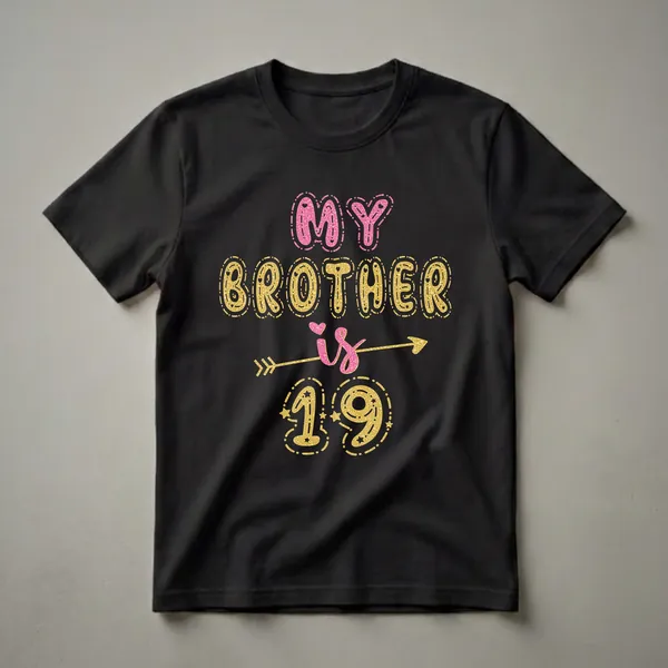 Black t-shirt with "MY BROTHER is 19" in glittery pink and gold bubble letters, accented by an arrow graphic.
