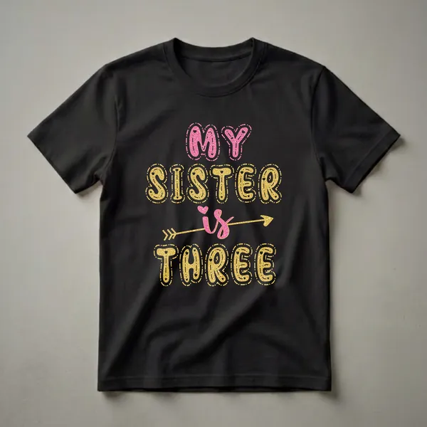 Black t-shirt with the text 'MY SISTER is THREE' in glittery pink and gold lettering, with a gold arrow and small pink hearts.