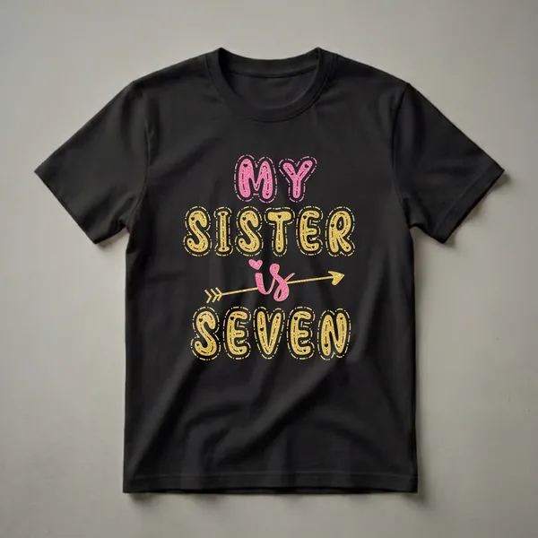Black t-shirt with "MY SISTER" in pink glittery letters and "is SEVEN" in gold glittery letters, with heart and arrow accents.