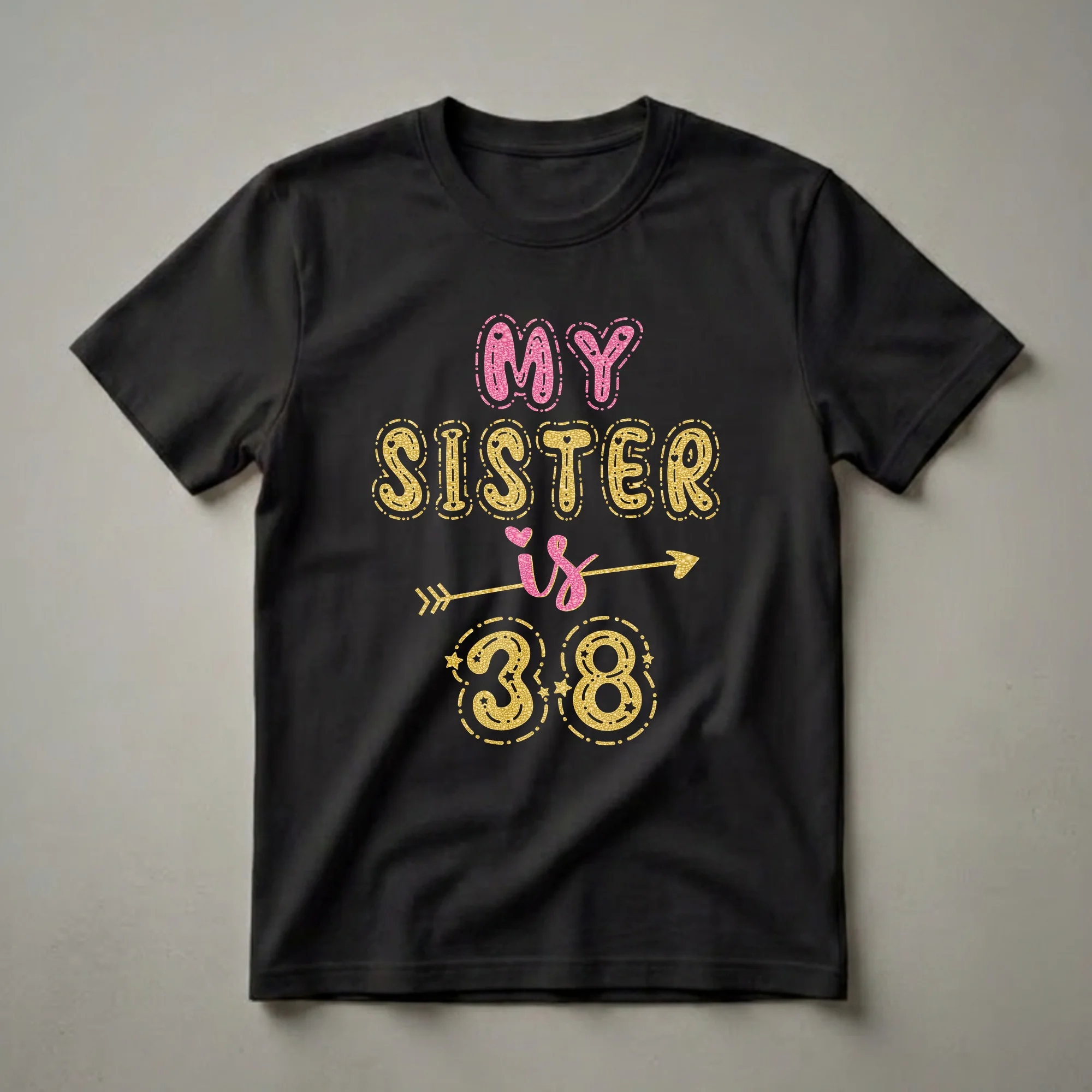 Black t-shirt with glittery pink and gold text that reads 'MY SISTER IS 38' with decorative elements like an arrow and stars.