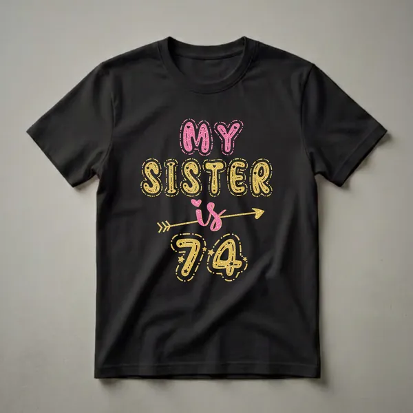 Black t-shirt with the text 'MY SISTER is 74' in pink and gold glitter-effect lettering, with decorative stars and an arrow.