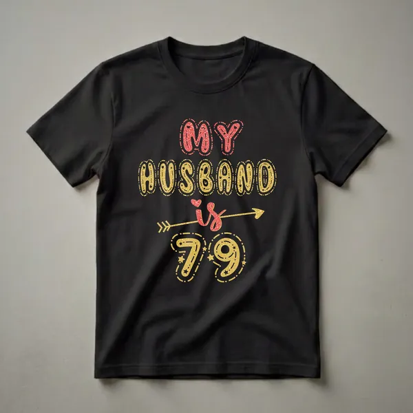 Black t-shirt with red and gold glitter text that reads 'MY HUSBAND is 79' with an arrow and stars.