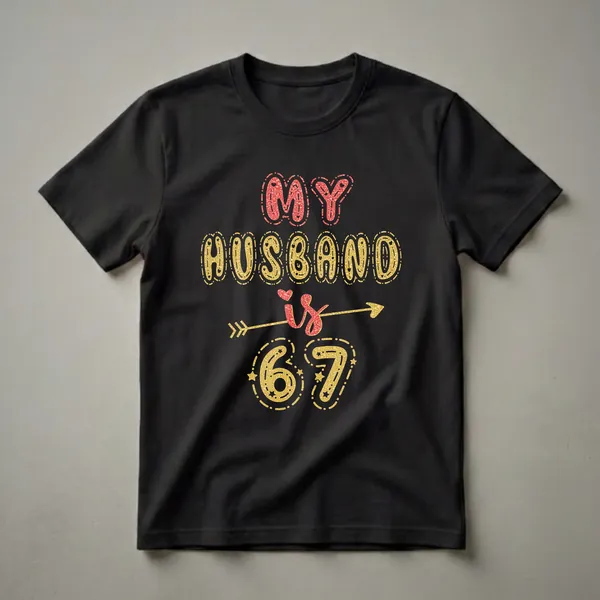 Black t-shirt with the text 'MY HUSBAND is 67' in glittery red and gold fonts, with decorative elements like hearts and arrows.
