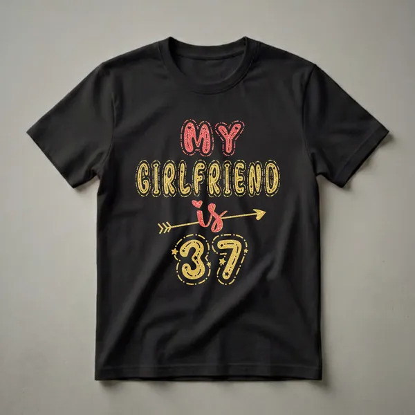 Black t-shirt with "MY GIRLFRIEND IS 37" in glittery red and gold fonts, featuring hearts, stars, and an arrow.