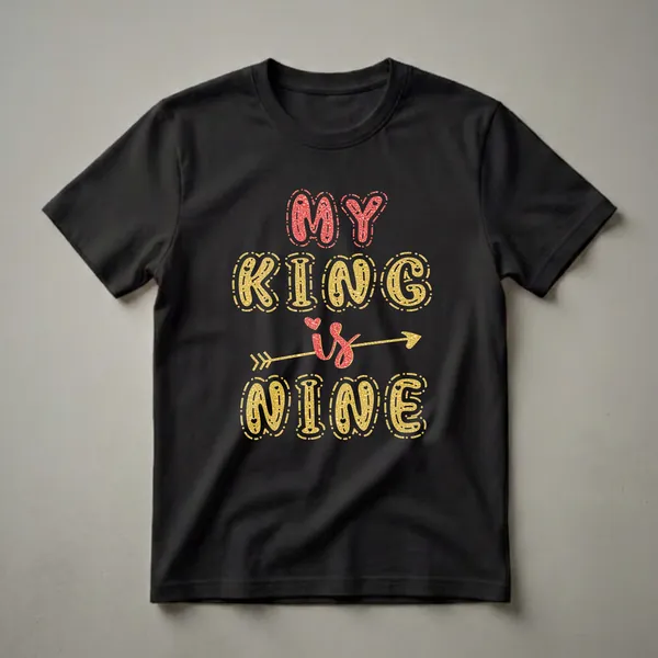 Black t-shirt with the text 'MY KING is NINE' in large, glittery gold and red bubble letters, with a red heart and gold arrow graphic.