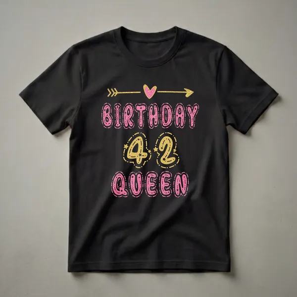 Black t-shirt with 'Birthday 42 Queen' text graphic. 'Birthday' and 'Queen' are in pink glittery letters, '42' is in gold glittery numbers. A gold arrow and pink heart are at the top.