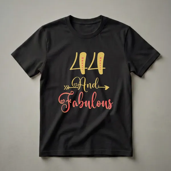 A white t-shirt graphic featuring the number 44 in gold glitter with red dots, and the words 'And Fabulous' in coral-red glitter script, framed by gold glitter arrows.