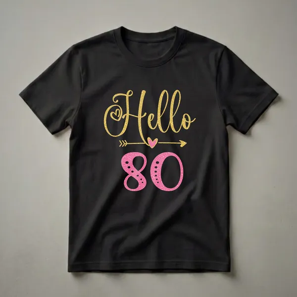 Black t-shirt with 'Hello 80' graphic. 'Hello' is in gold glitter font with a heart and arrow, and '80' is in a pink bubble texture.