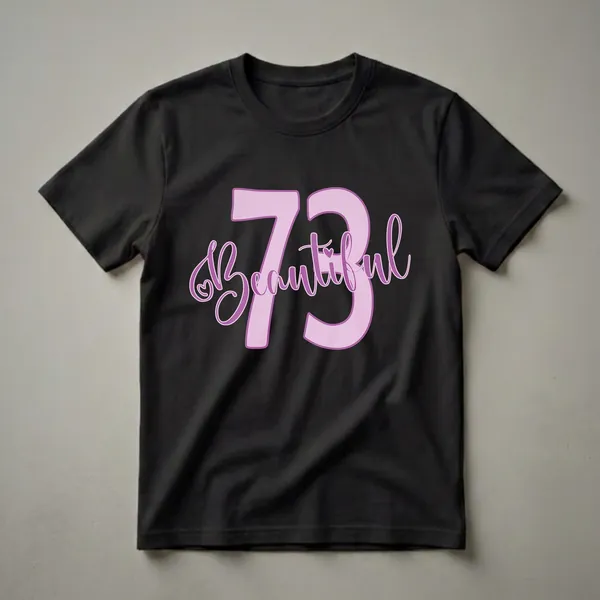 A graphic t-shirt design featuring the number 73 in large pink font with the word 'Beautiful' in purple script, and a small heart detail. The design is on a black background.