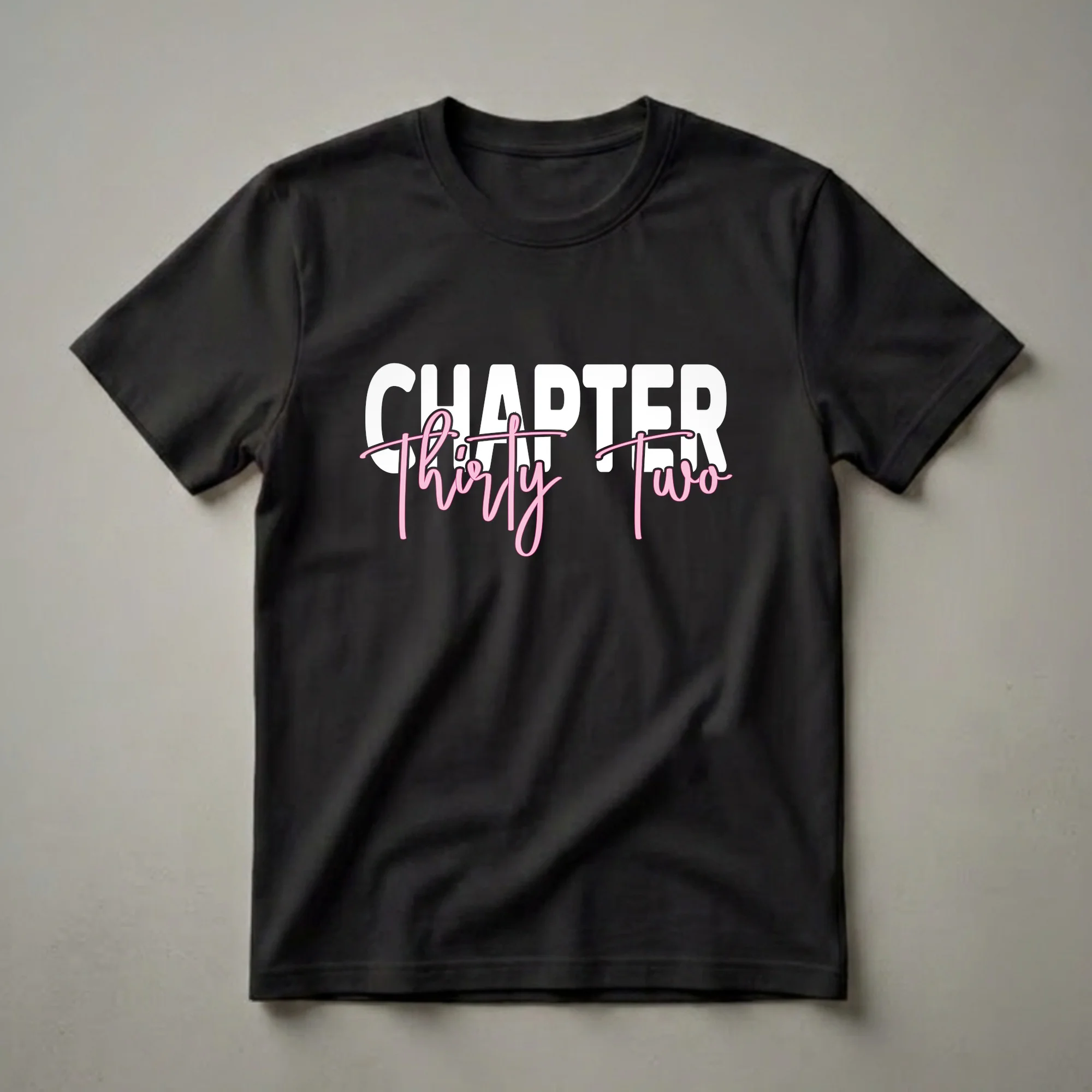Black t-shirt with white block text 'CHAPTER' above pink script text 'Thirty Two', celebrating a 32nd birthday.
