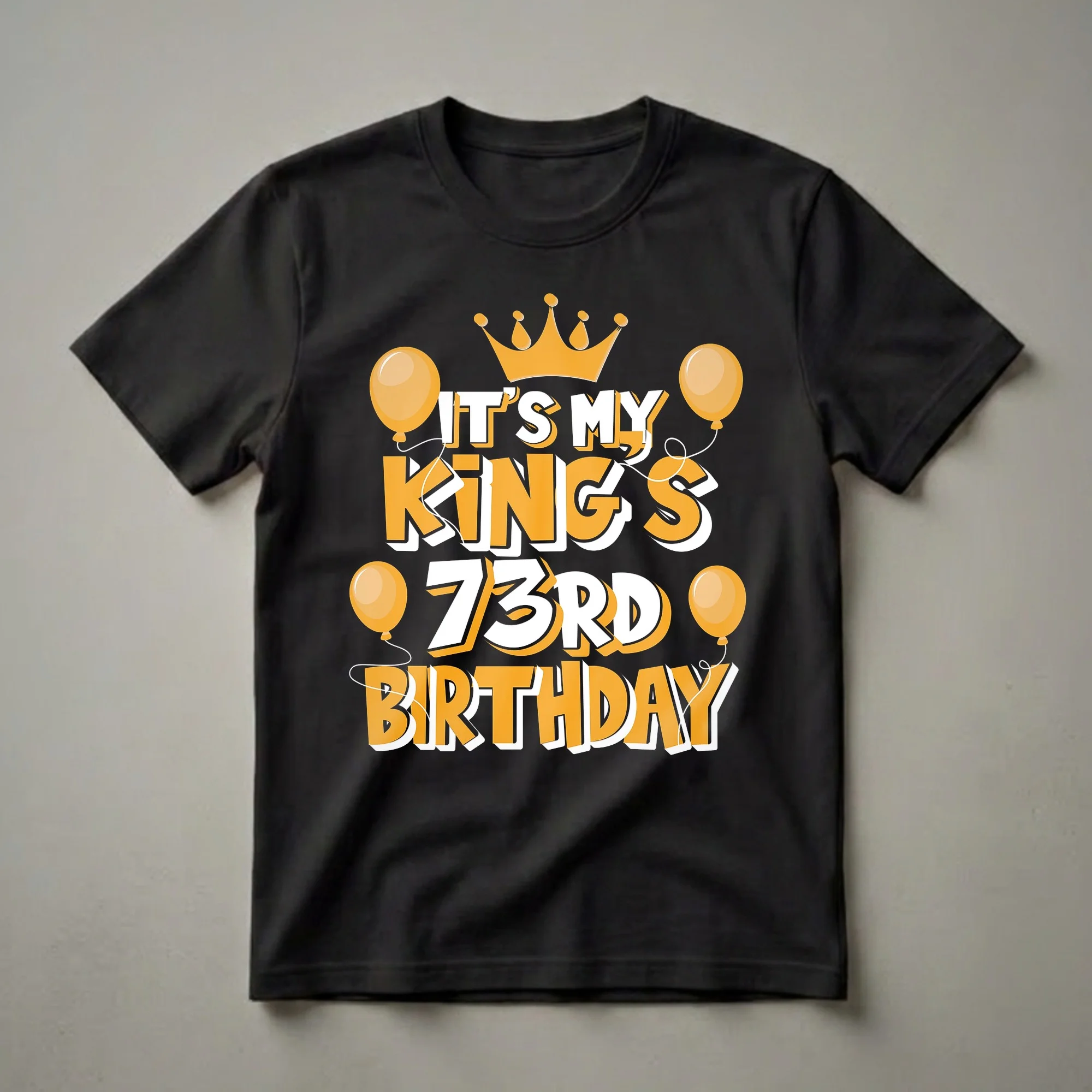 Black t-shirt with orange and white text reading 'IT'S MY KING'S 73RD BIRTHDAY', topped with a crown and surrounded by balloons.