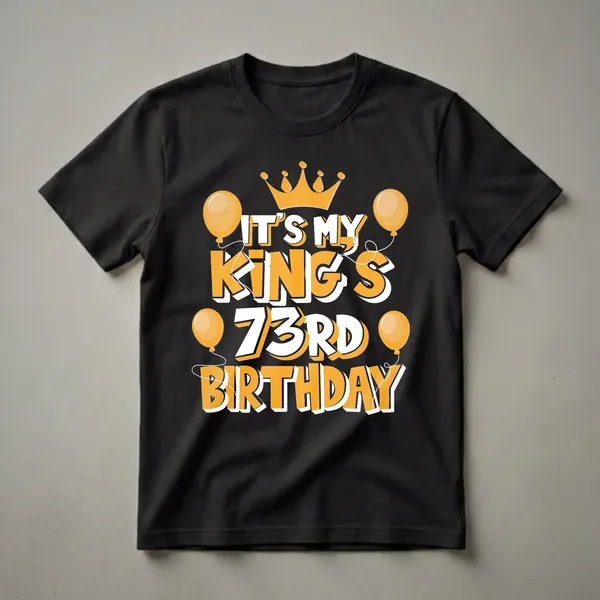 Black t-shirt with orange and white text reading 'IT'S MY KING'S 73RD BIRTHDAY', topped with a crown and surrounded by balloons.