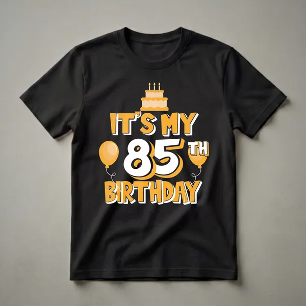 Black t-shirt with orange and white text that reads 'IT'S MY 85TH BIRTHDAY', featuring a birthday cake with candles and two balloons.