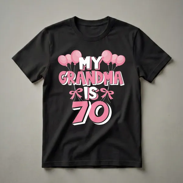 Black t-shirt with the text "MY GRANDMA IS 70" in large pink and white bubble letters, adorned with pink balloons and pink bows.